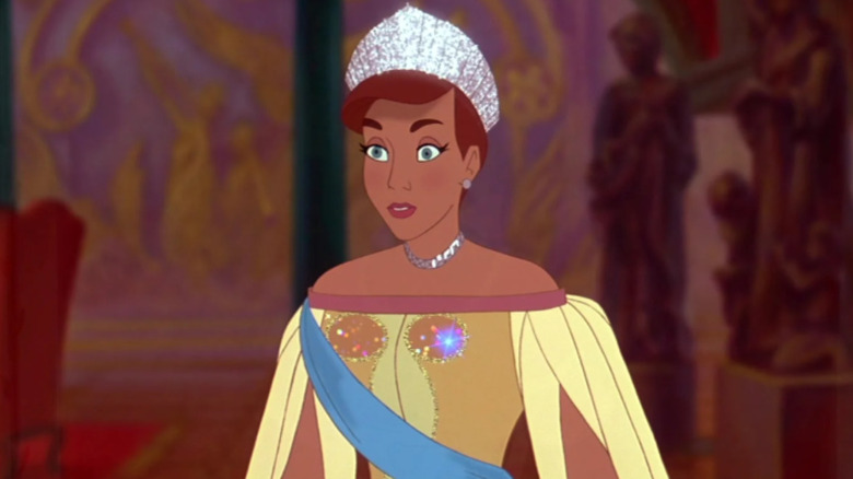 Anastasia standing in room while wearing a diamond crown and yellow gown with a blue sash