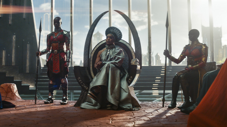 Ramonda on the Wakandan throne, flanked by Ayo and Okoye