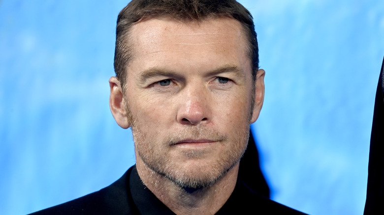 Sam Worthington in front of blue background