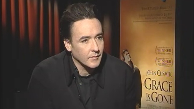 John Cusack sitting with a student interviewer in front of the Grace Is Gone movie poster