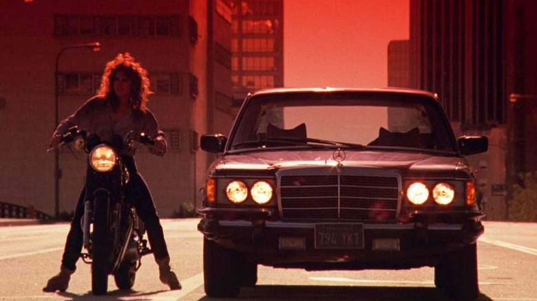 Reggie sits on a motorcycle next to a parked car in Night of the Comet (1984)