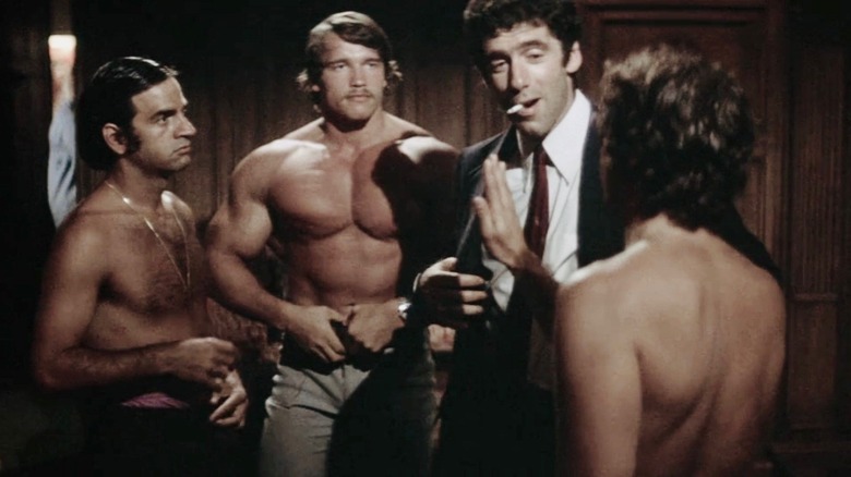 Philip Marlowe stands with a cigarette in his mouth as three buff, shirtless men encircle him