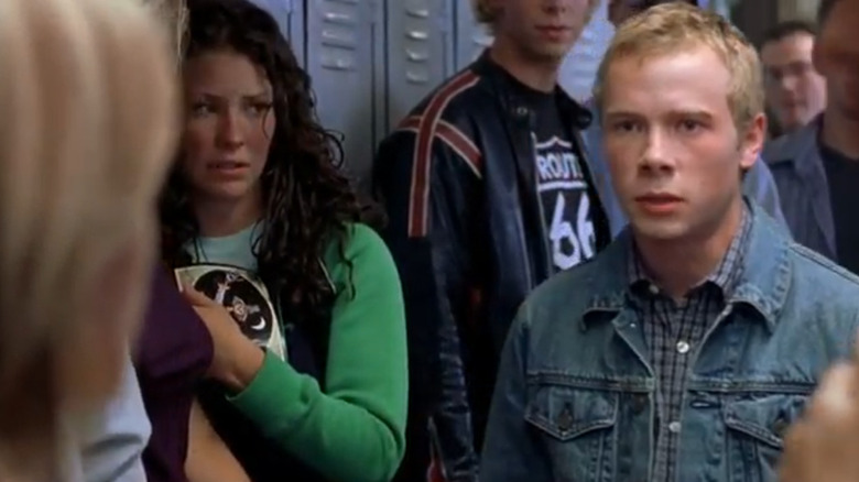 A crowd of teens stand in front of lockers in a high school hallway