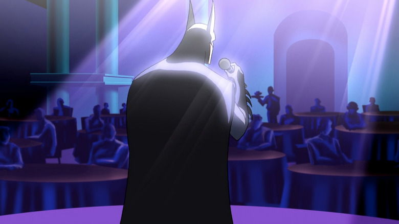 Batman sings with a microphone while facing an audience