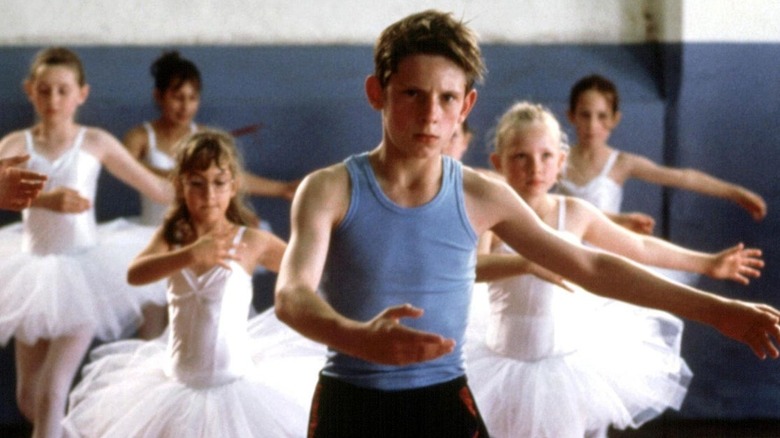 A young boy dances surrounded by girls in ballet tutus