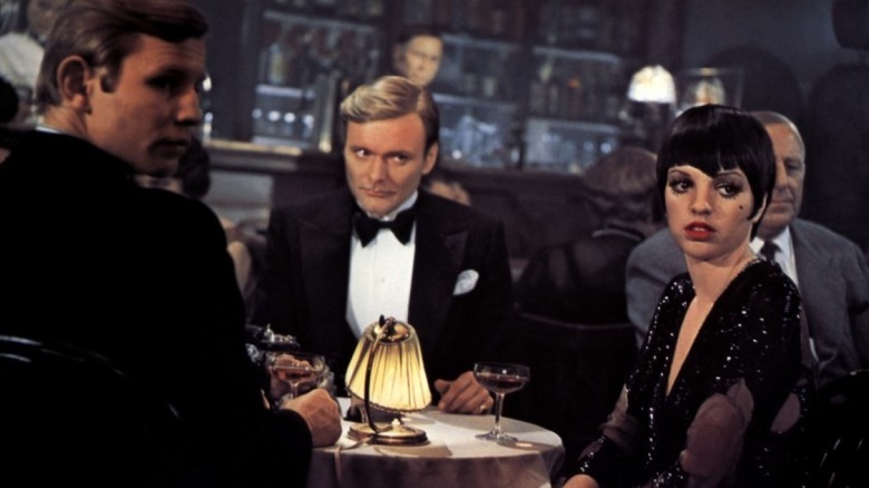 Two men and a woman in a '30s bar scene stare intently off-camera