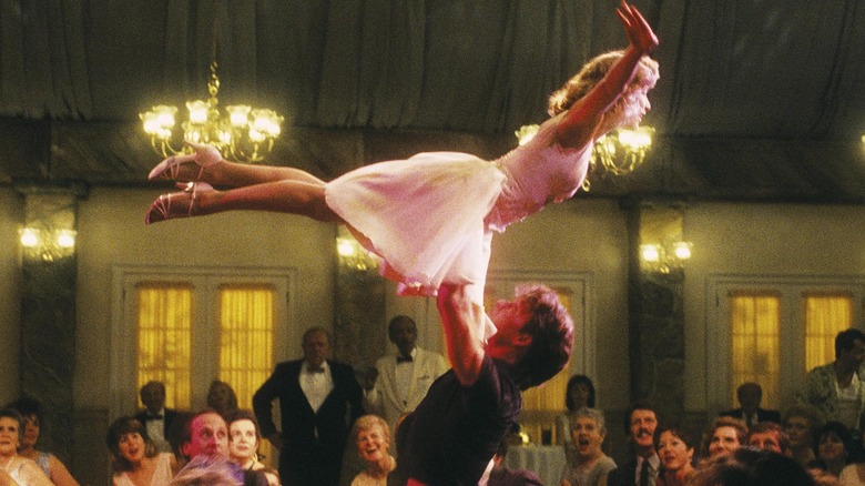 A man lifts a woman in the air on a dance floor while a crowd watches