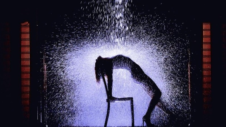 A woman is silhouetted with her back arched under falling water