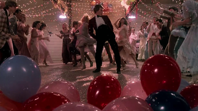 Several young people dance while surrounded by balloons and string lights