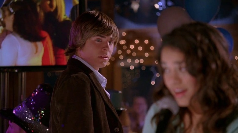 A young man gazes at a young woman with a party in the background