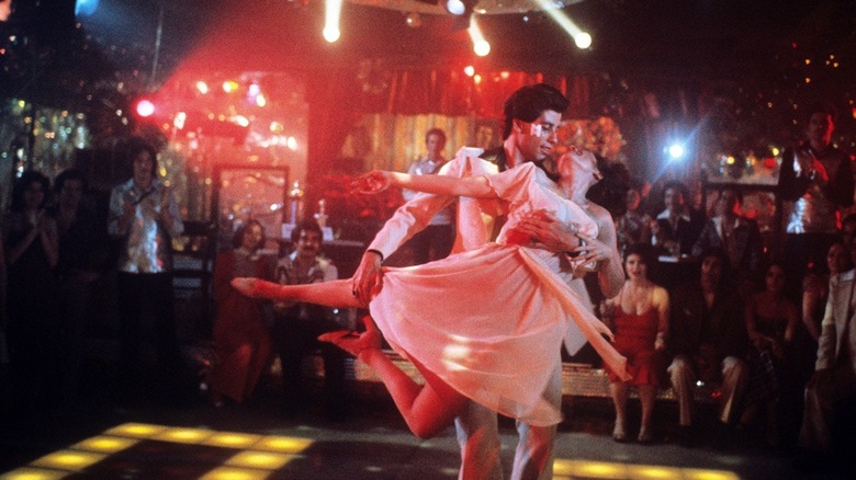 A man and a woman in white twirl on a lighted disco dance floor