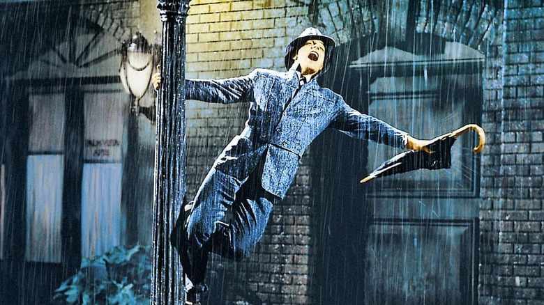 A man with an umbrella swings from a lamppost in the rain