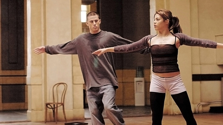 A man and a woman stand with their arms outstretched in a dance classroom