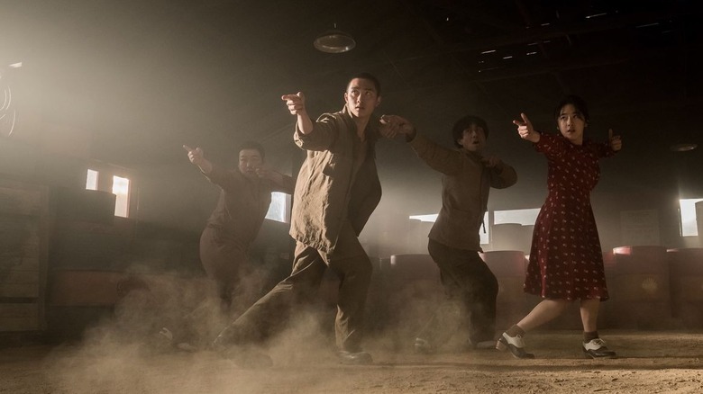 Four people kick up dust as they perform a synchronized dance routine