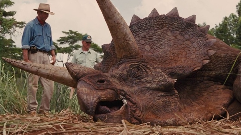 Two men standing beside dead triceratops