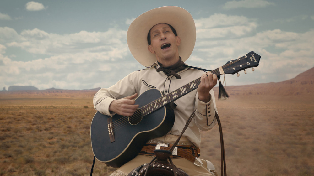 Buster Scruggs singing on horse with guitar