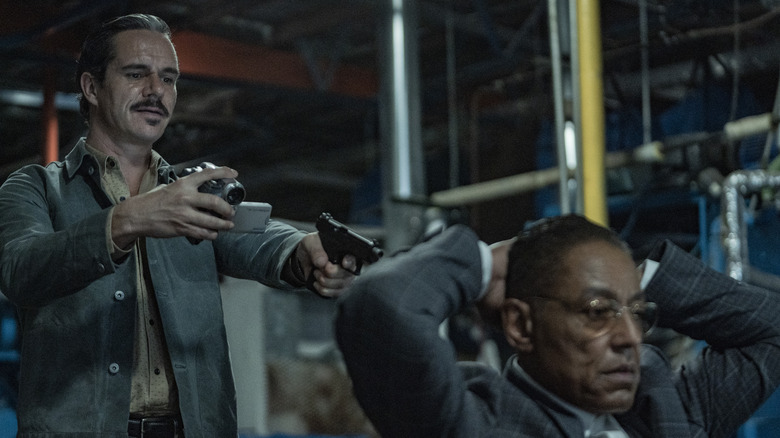 Lalo Salamanca points a gun and a camera at Gus Fring