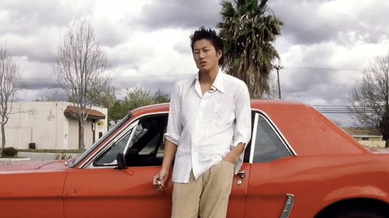 Han stands next to red car while