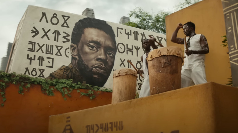 Wakandan drum players next to mural of T'Challa in Black Panther: Wakanda Forever