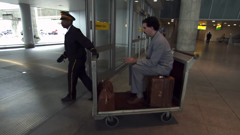 Airport bellman pulling Borat on luggage trolley