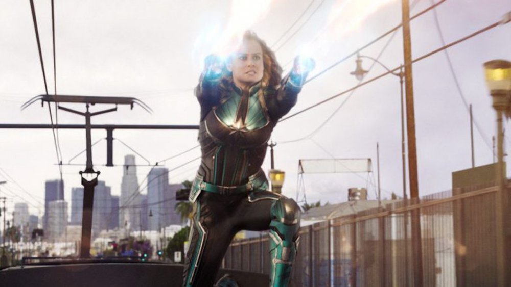 Captain Marvel shoots photonic light beams from her hands from the top of a train