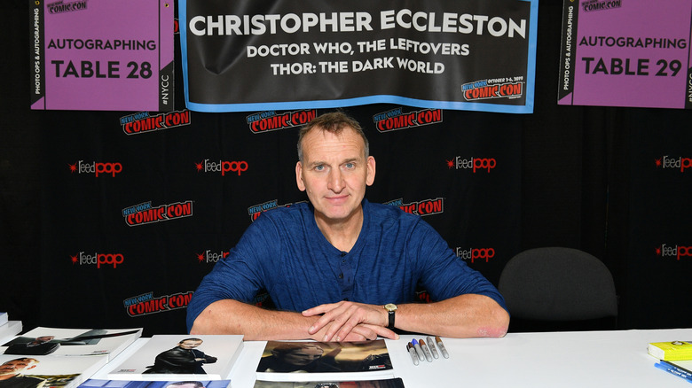 Eccleston sits at a table