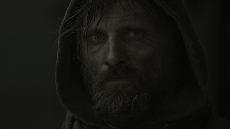 A hooded man looks haunted in close-up