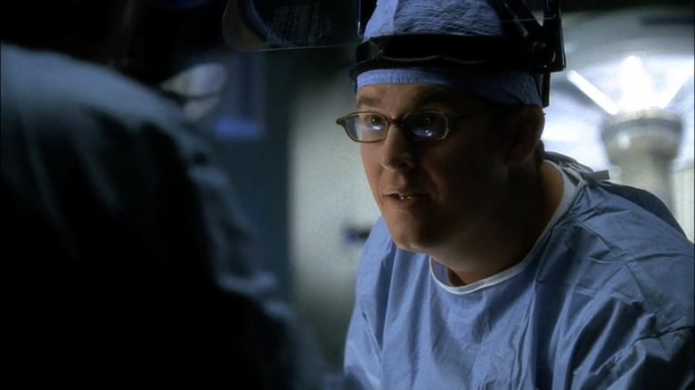 David Philips wearing blue medical scrubs, glasses, and a face shield on his head
