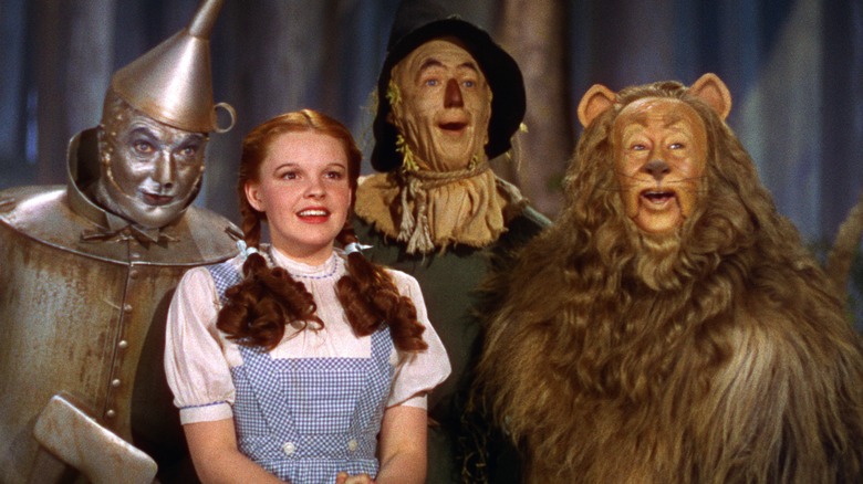 The tin man, Dorothy, scarecrow, and lion standing together