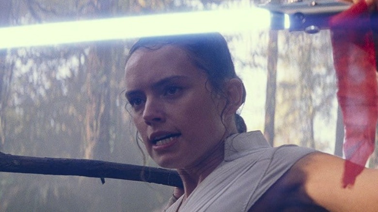 Rey holding a lightsaber and a stick