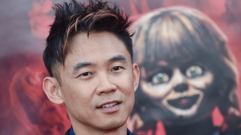 James Wan standing in front of an Annabelle poster