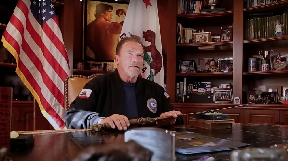 Arnold Schwarzenegger sitting at desk with Conan sword