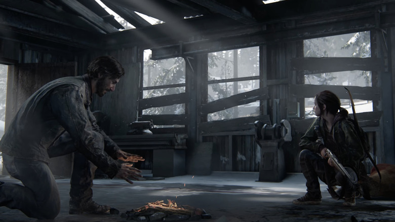 David warms his hands over a fire while Ellie watches with a gun