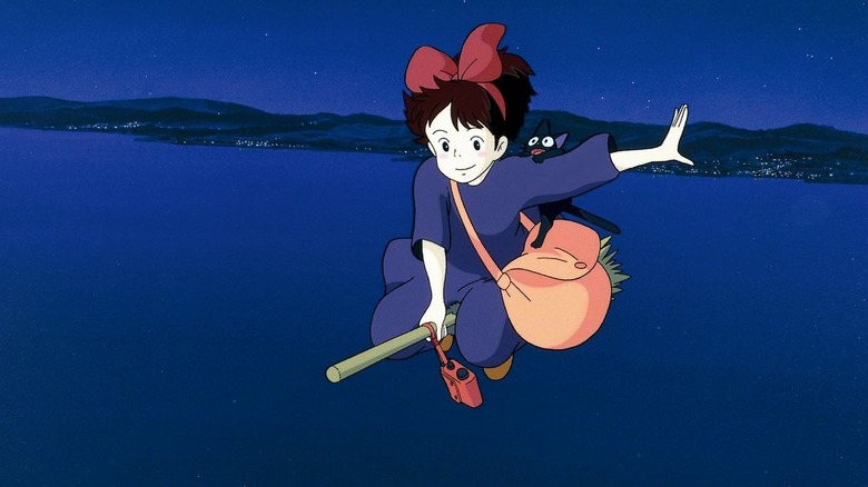 Kiki flies on her broom, with Jiji hanging on her arm