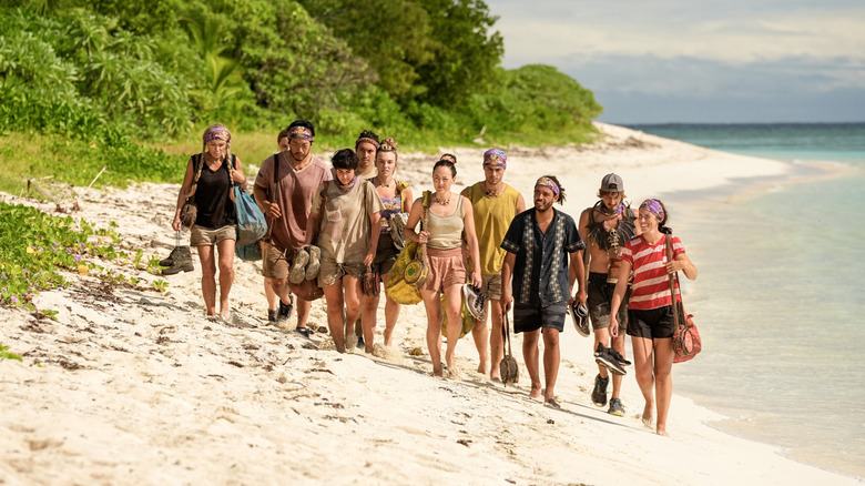 A group of "Survivor" Season 47 contestants walk on the beach together carry their bags