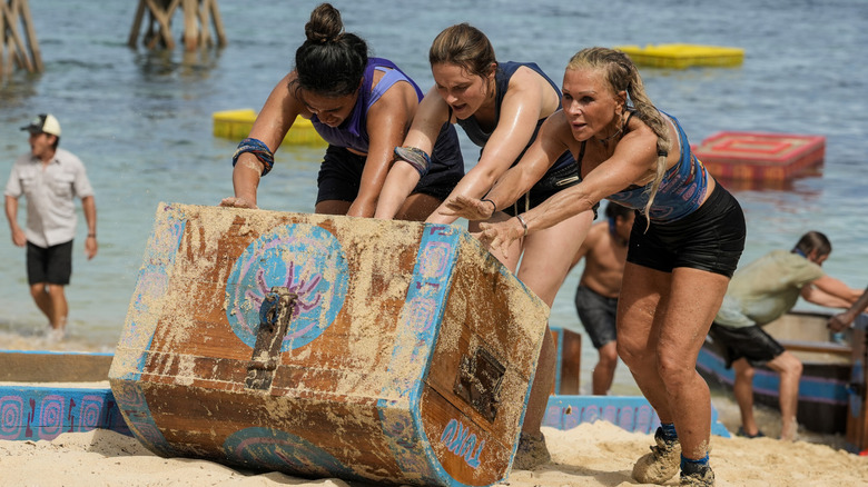 Tiyana Hallums, Caroline Vidmar, and Sue Smey roll a treasure chest together