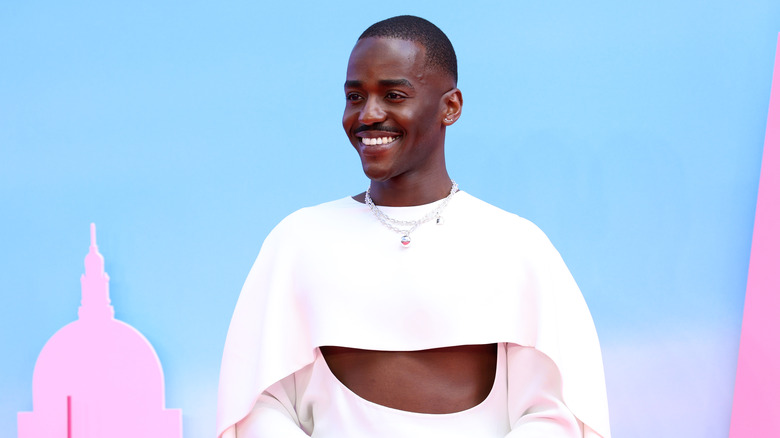 Ncuti Gatwa with arms folded in front of a pink and blue Barbie display