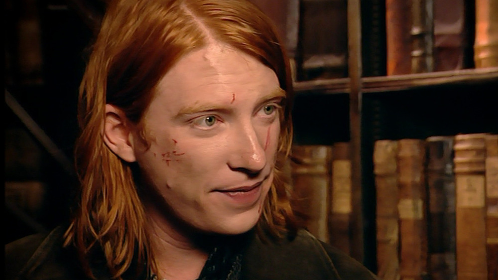 Bill Weasley standing next to a book case