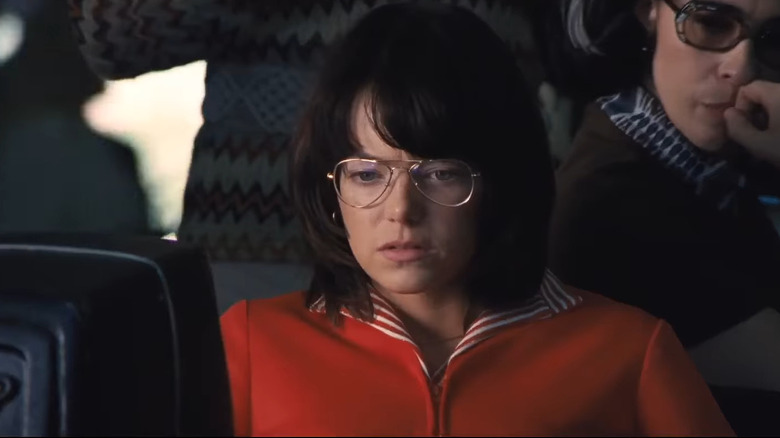 Stone with dark hair and glasses in red jacket