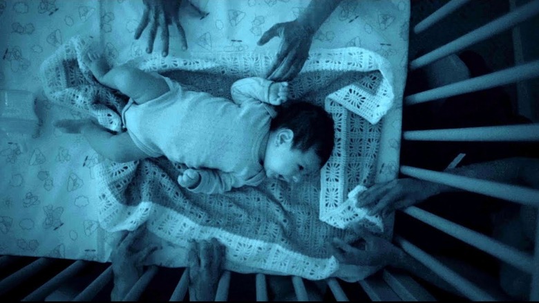 Hands surround infant in crib