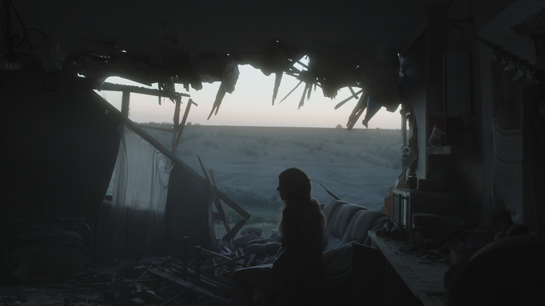 Woman sits by destroyed wall