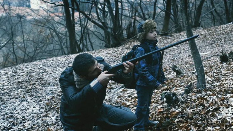 A man aims a gun next to boy