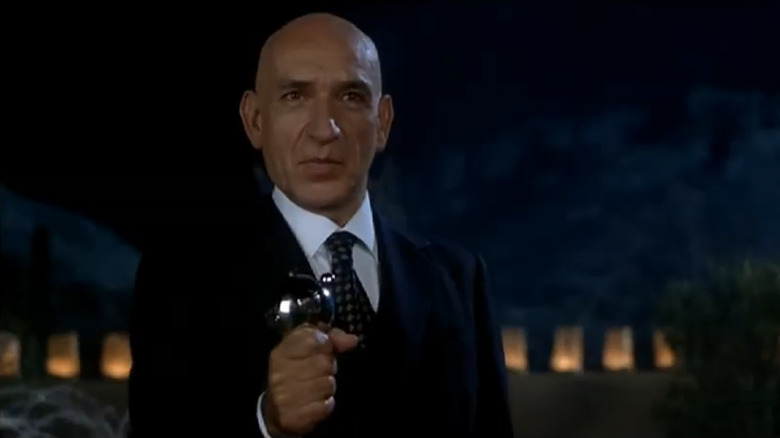 Ben Kingsley in a suit holding a device