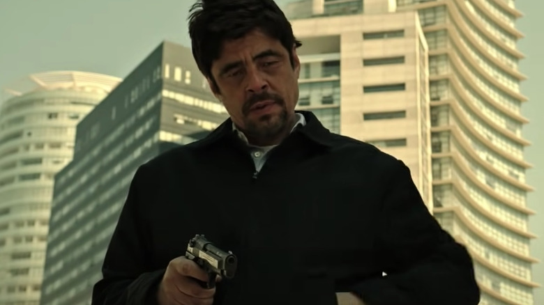 Benicio Del Toro holding gun outside