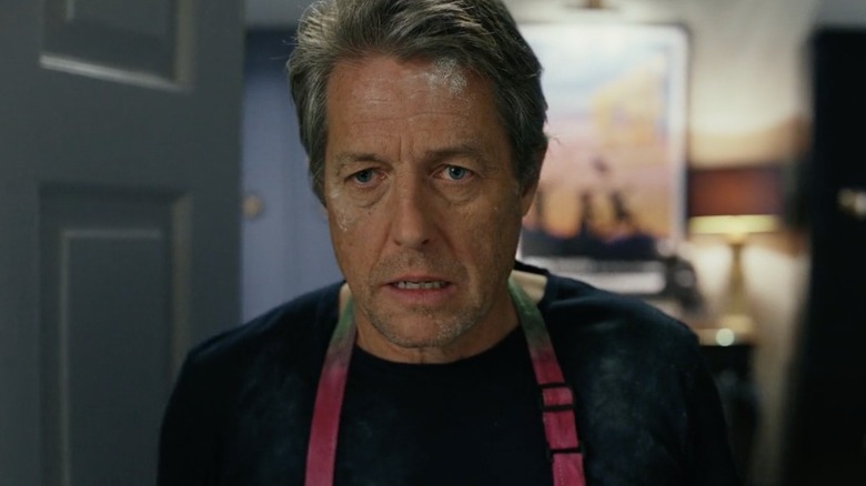 Hugh Grant covered in flour wearing a pink apron