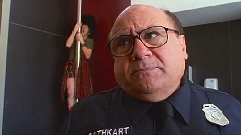 A man slides down a pole behind Danny DeVito