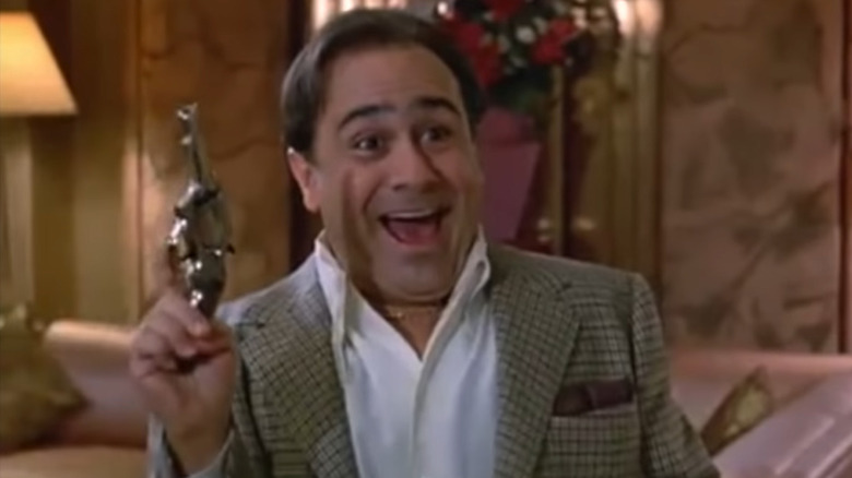 Danny DeVito holds a gun and smiles