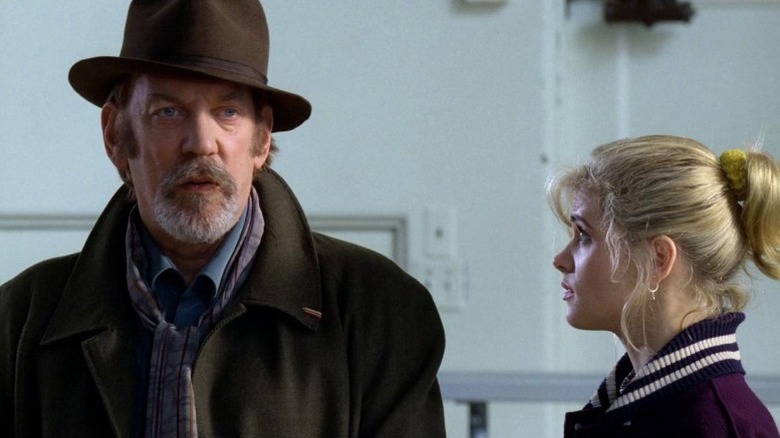 Donald Sutherland in coat and fedora talking to Kristy Swanson