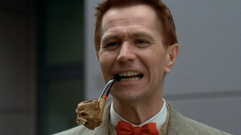 Gary Oldman smiles while smoking a pipe