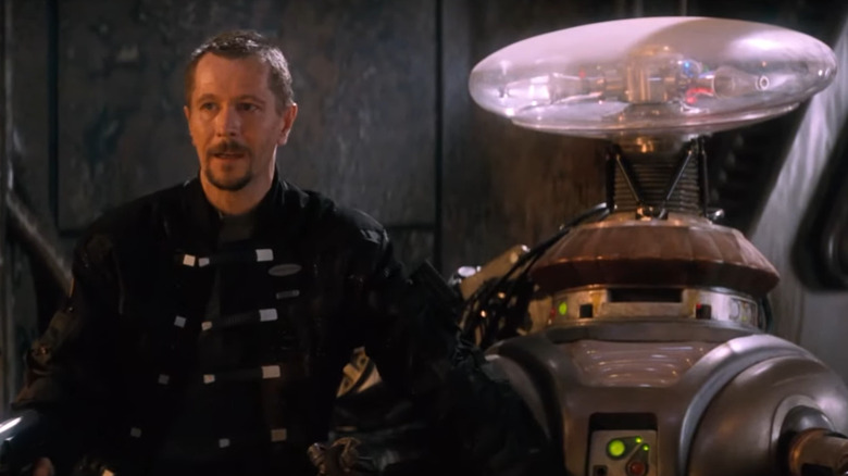 Gary Oldman stands next to a robot